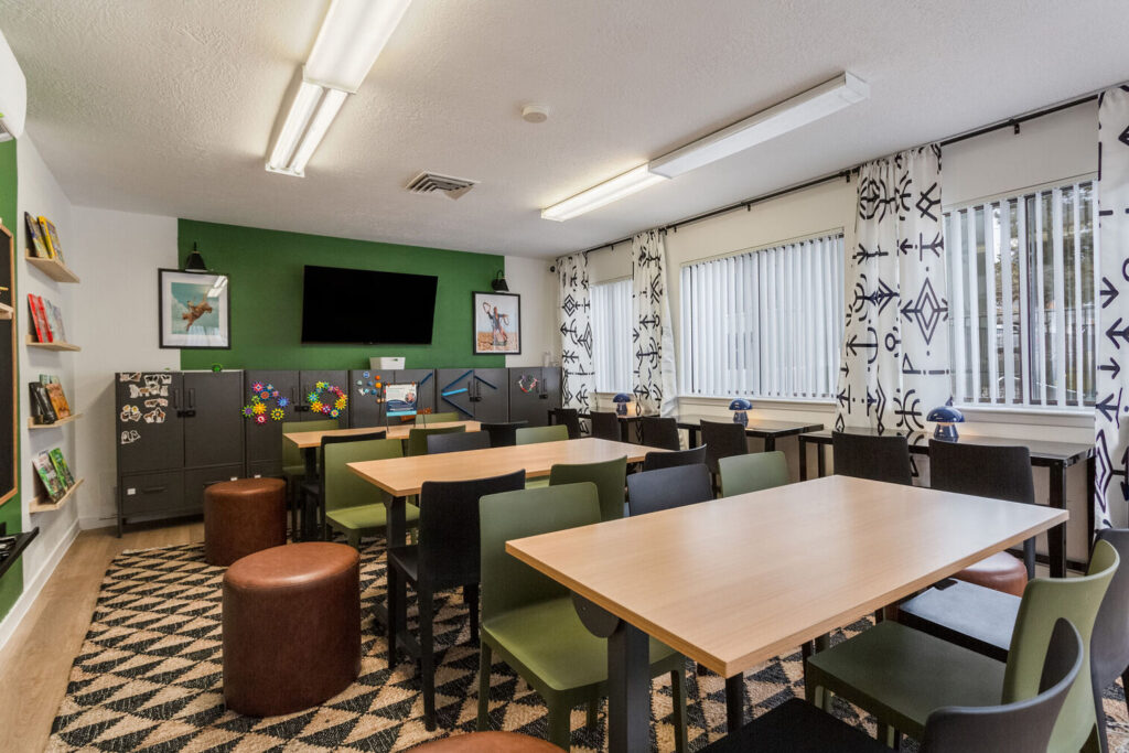Kids club with desks and chairs, large windows, and shelves with books and games
