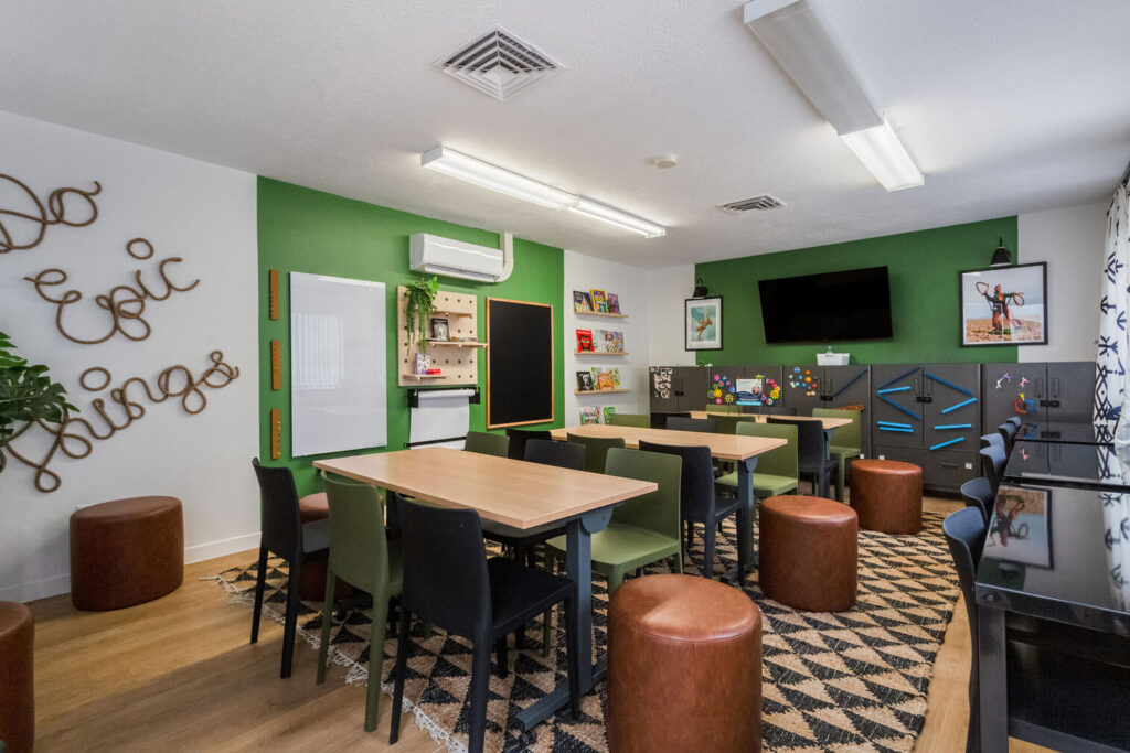 Kids club with desks and chairs, large windows, and shelves with books and games