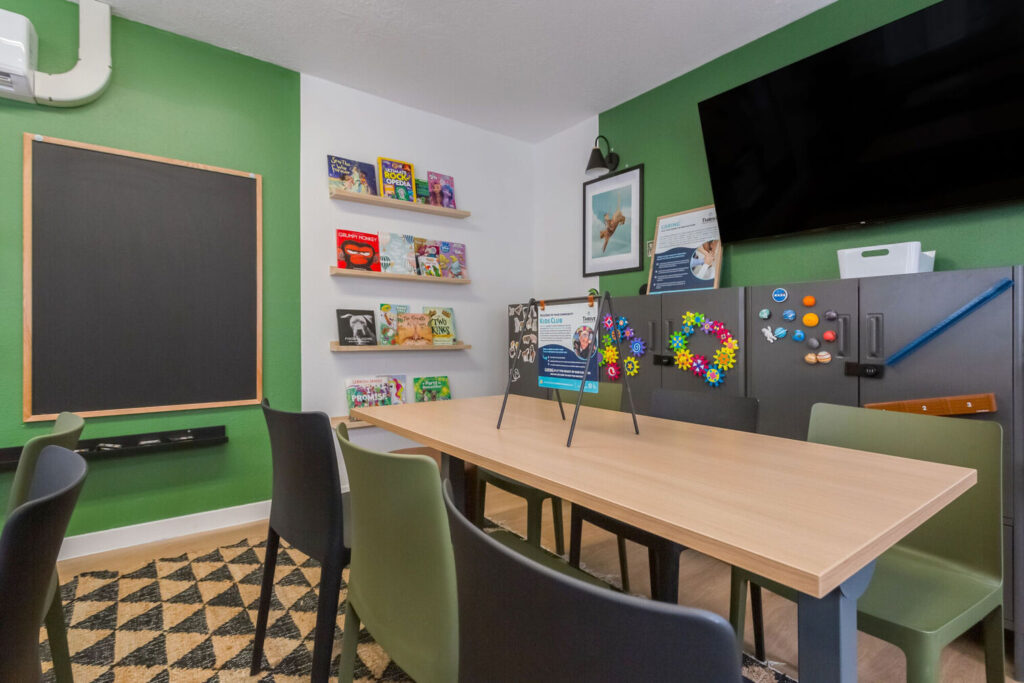 Kids club with desks and chairs, large windows, and shelves with books and games